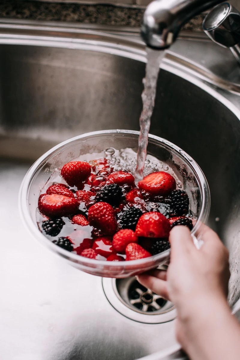 berries in a bowl being washed under the sink