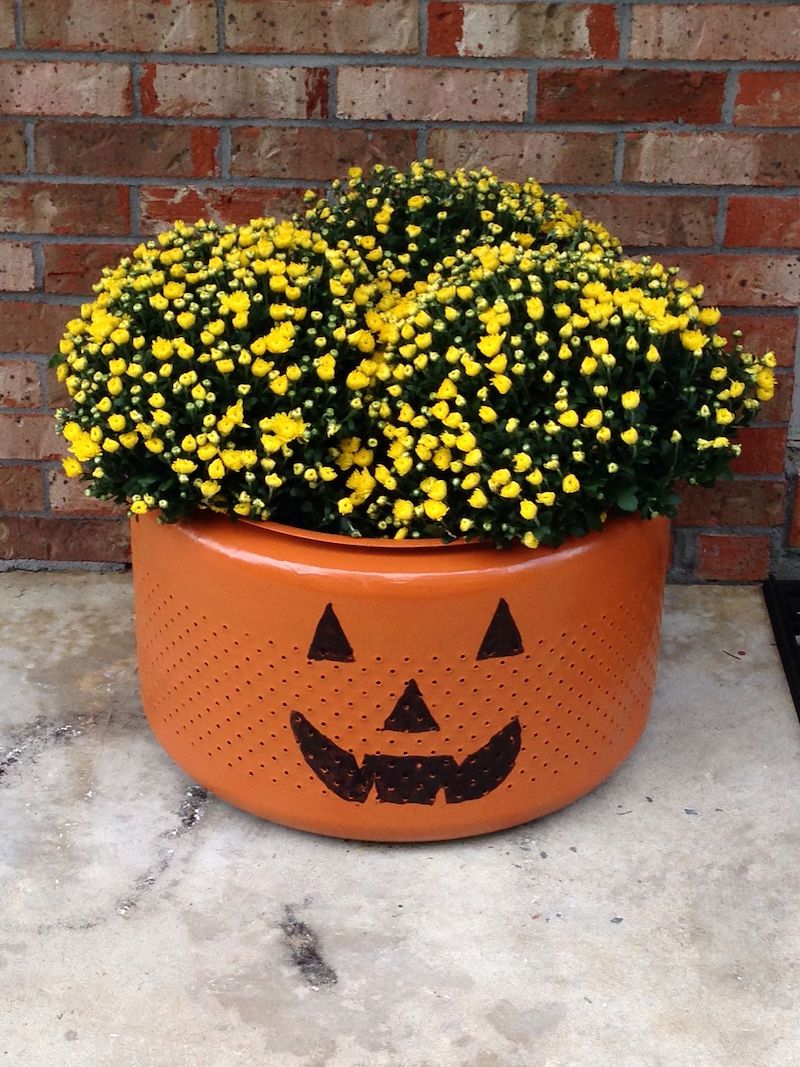 halloween painted pumpkin on old washing machine drum with yellow flowers