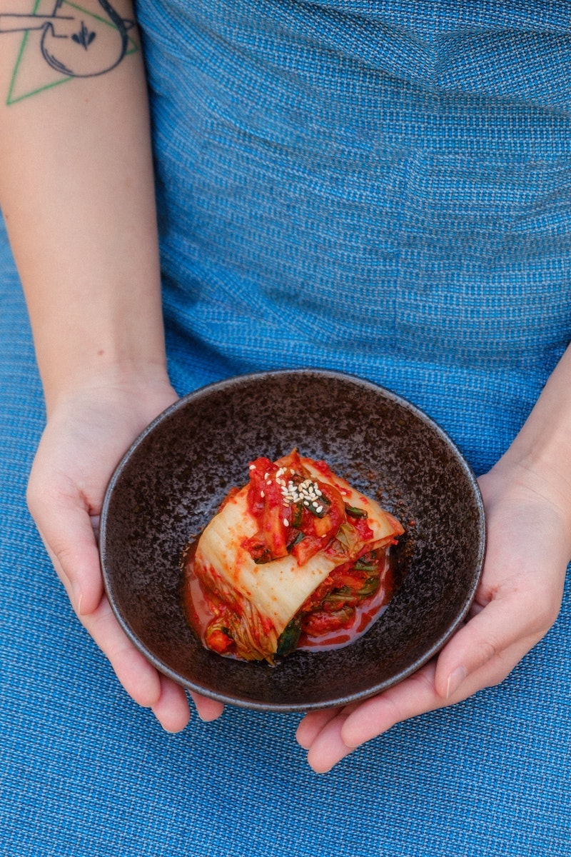 osoba w niebieskim fartuchu trzymająca kimchi w misce