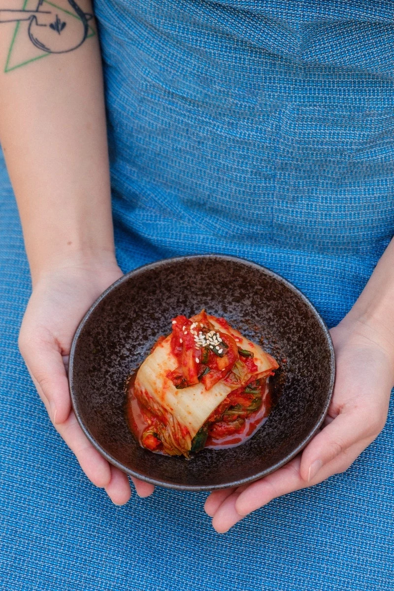 person with blue apron holding kimchi in a bowl