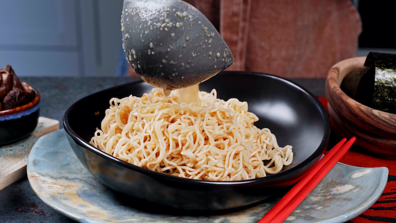 ramen in a black bowl with broth in a ladle