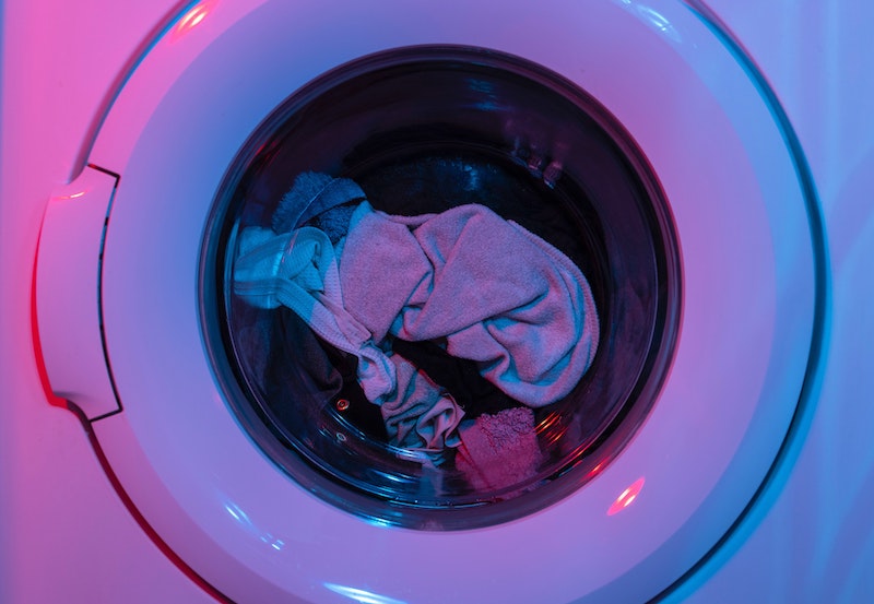 washing machine door closed with laundry inside in pink and purple light