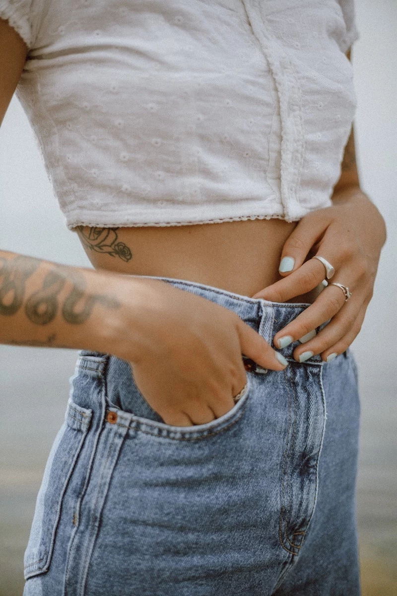 woman in jeans and white crop top tocuhing her stomach
