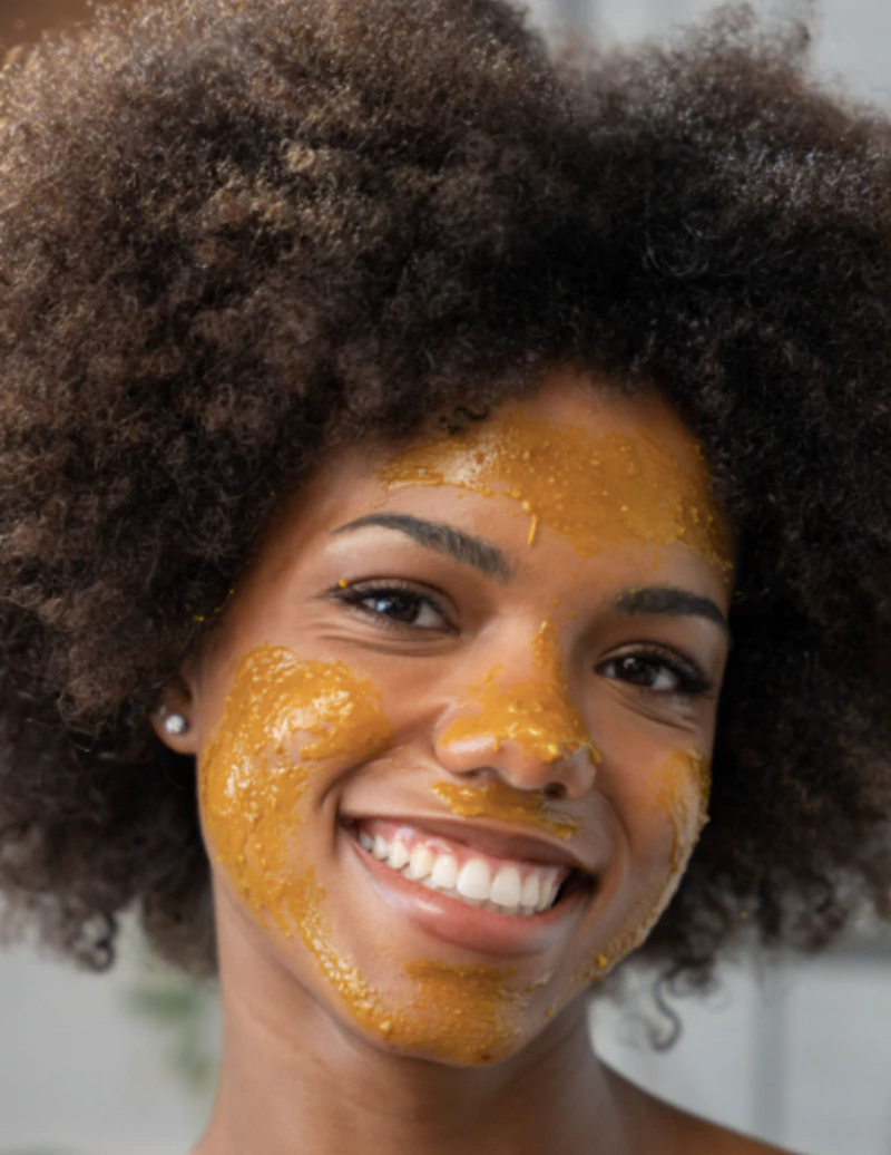 woman smiling with turmeric and honey face mask on