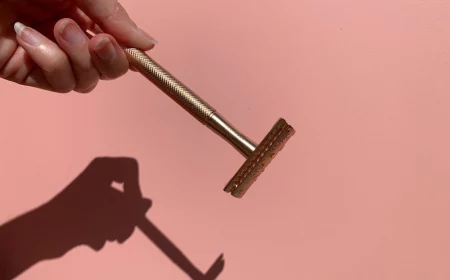 alternatives to shaving hand holding golden razor on pink background