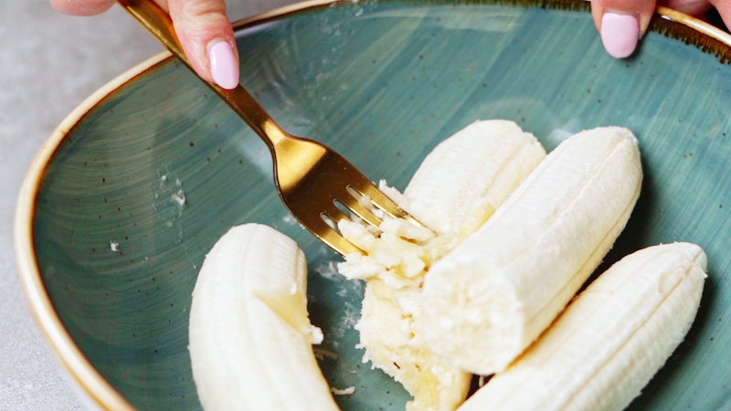 plátanos en un plato verde, triturados con un tenedor