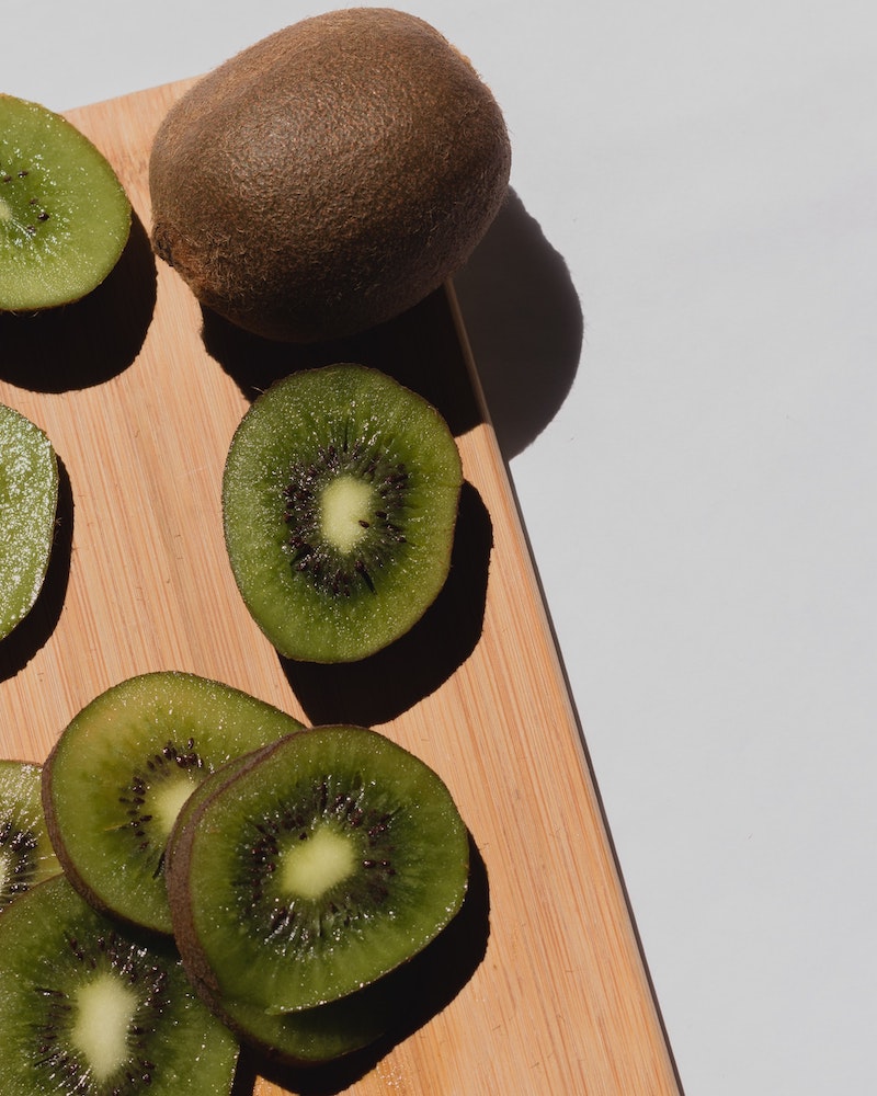 cut kiwi and whole kiwi on wooden board
