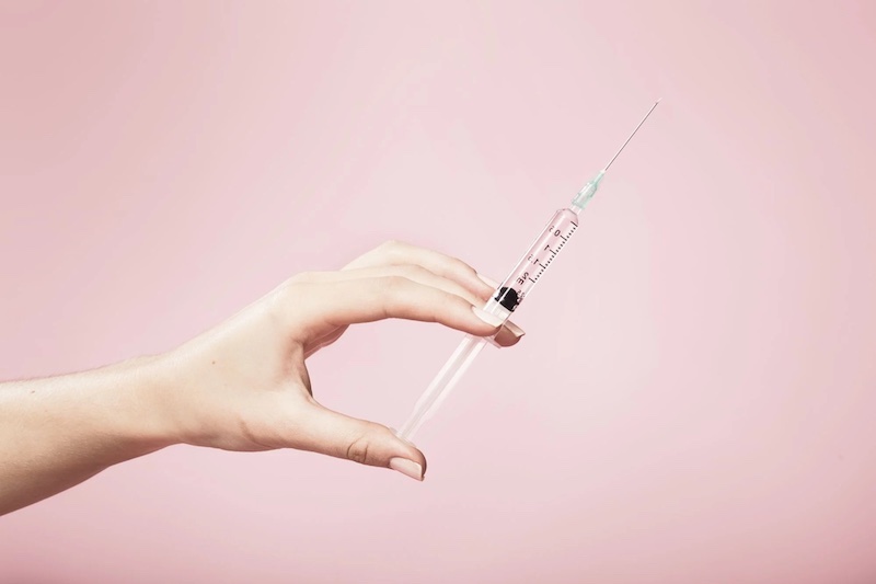 hand holding needle of botox on pink background