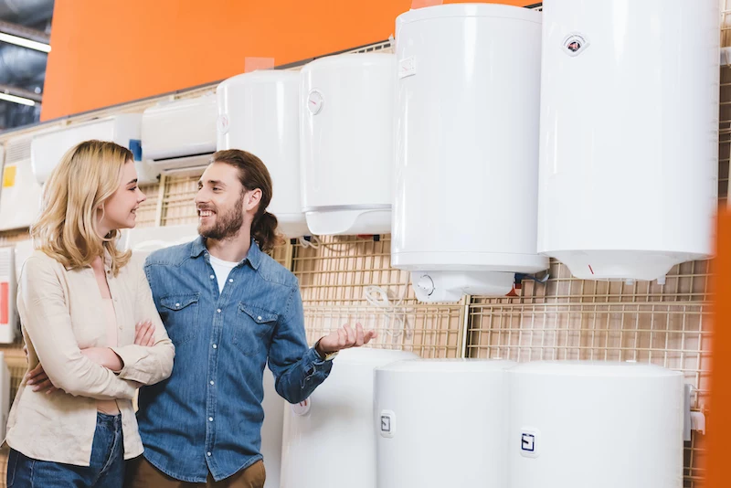 smiling boyfriend and girlfriend talking near boilers in home appliance store