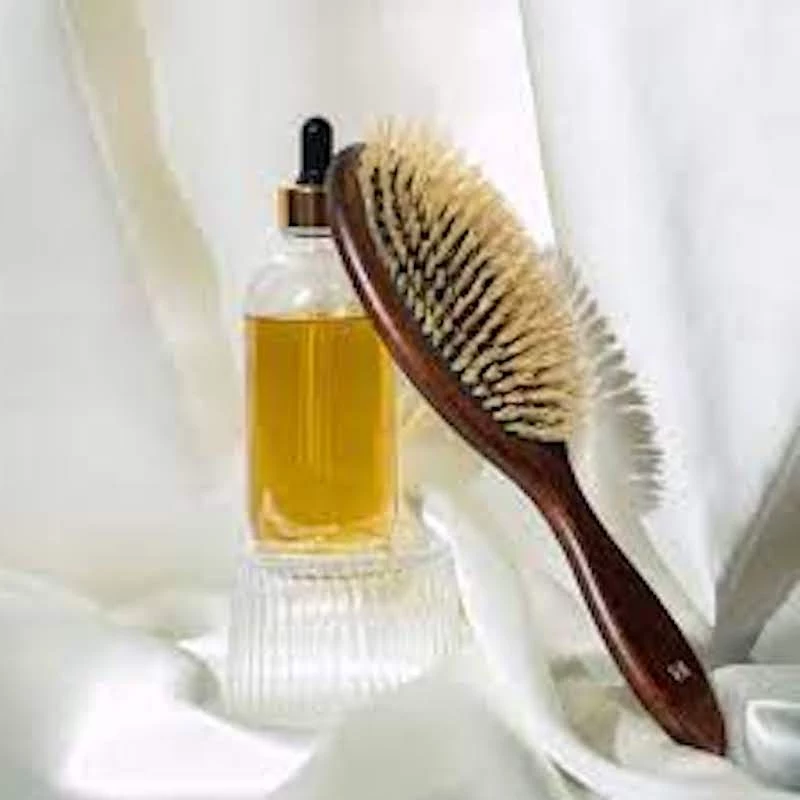 oil in a glass bottle next to a hair brush