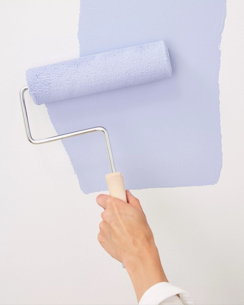 person with a paint roller painting a wall blue