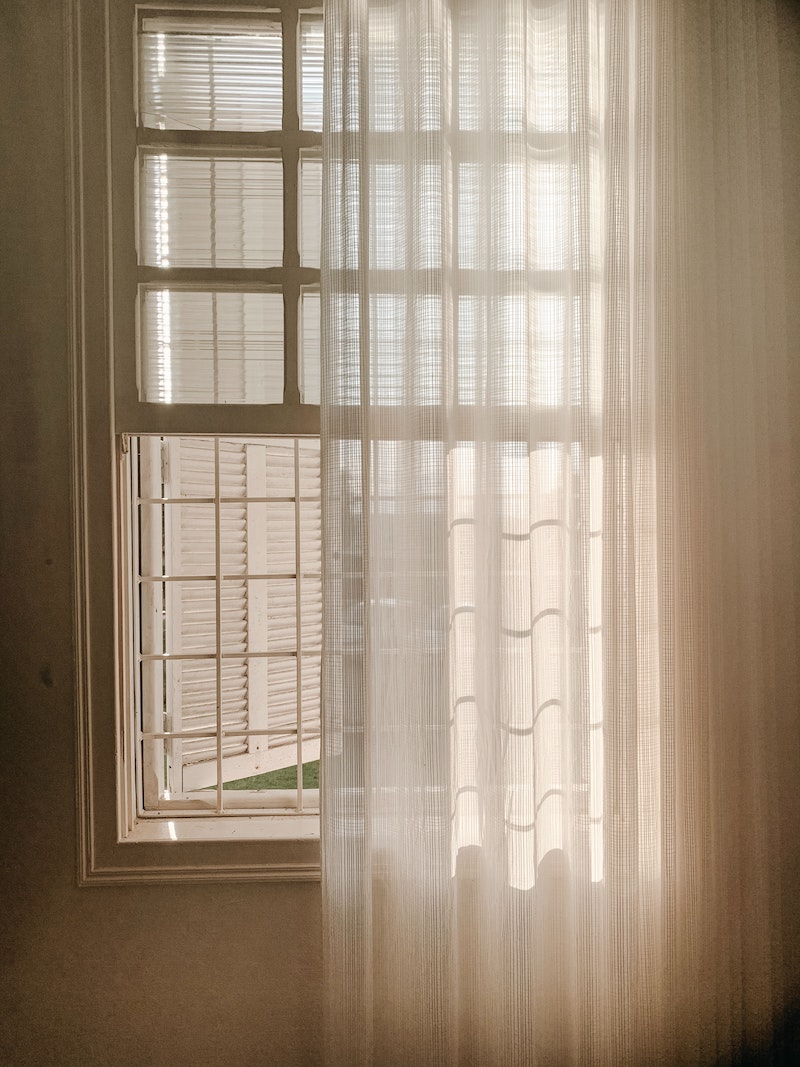 una ventana blanca con una cortina corrida a la mitad de la ventana