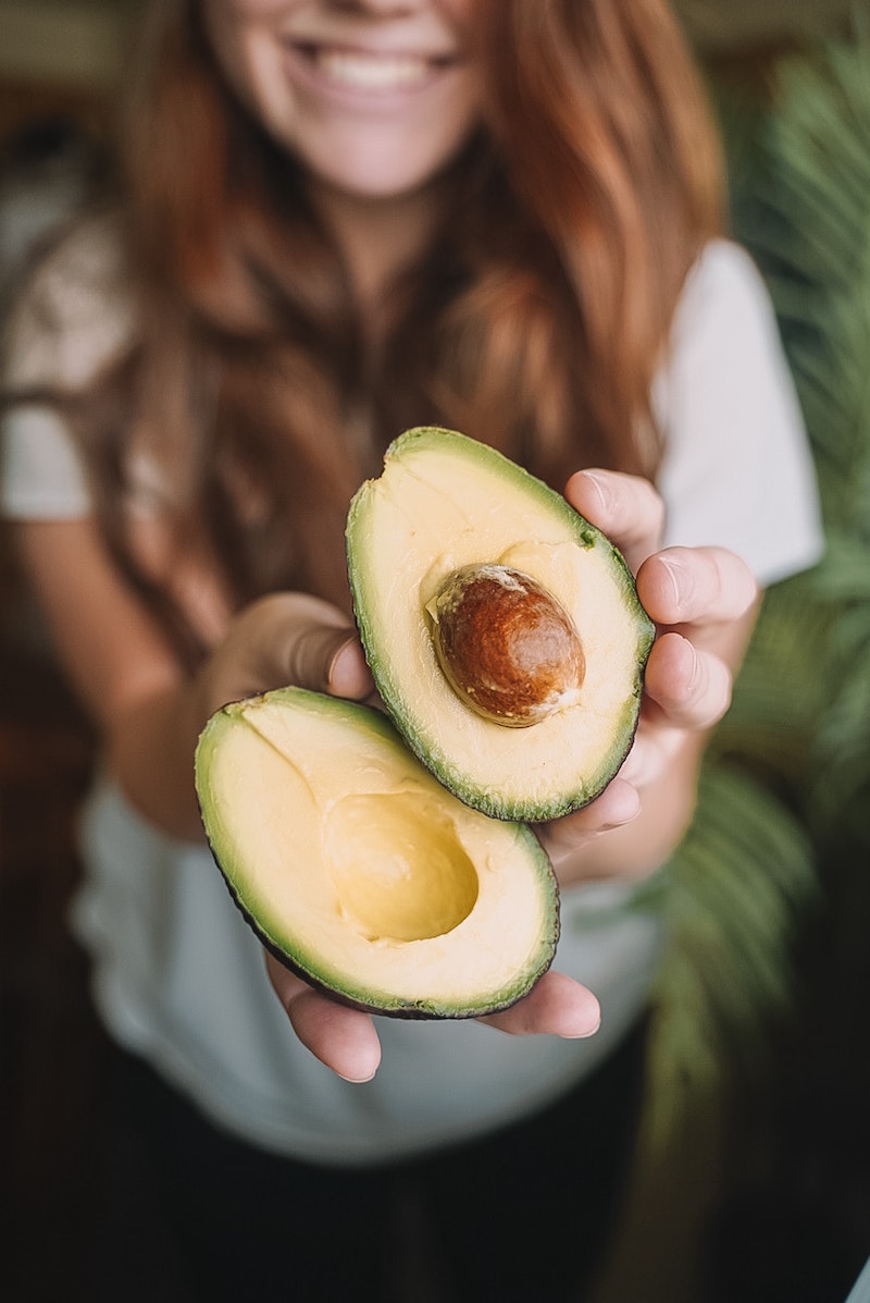 woman holding a sliced avocado and smiling