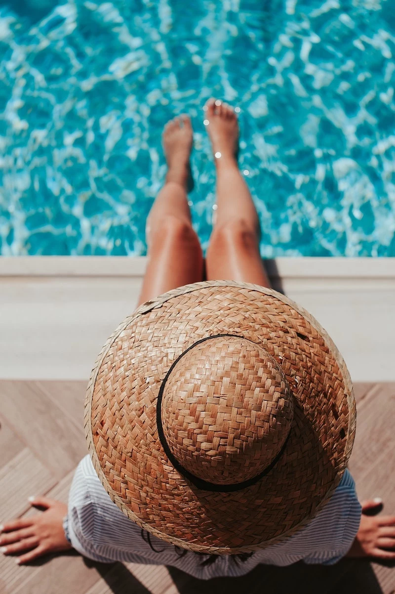 woman in a sun hat sitting on the side of the pool