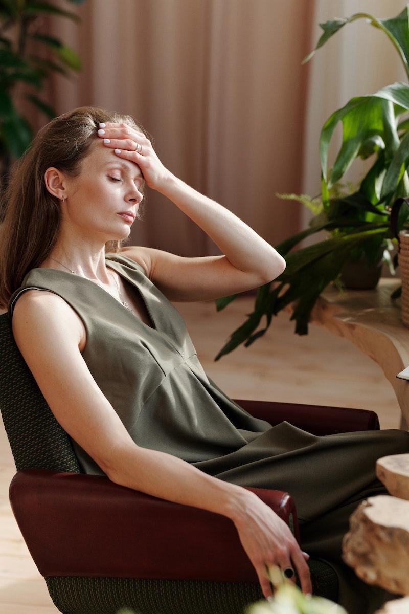 woman sitting on a chair holding her forhead