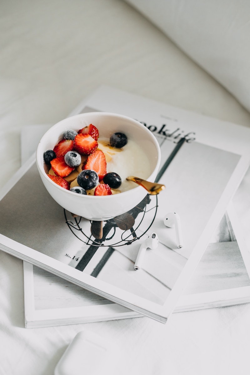 bowl of yogurt with fruits on magazine with airpods