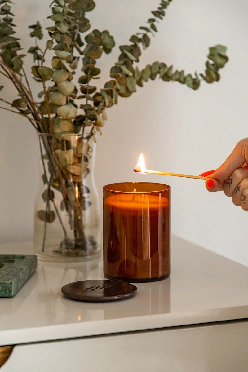 candle being lit with matchstick with eucalyptus leaves in the background