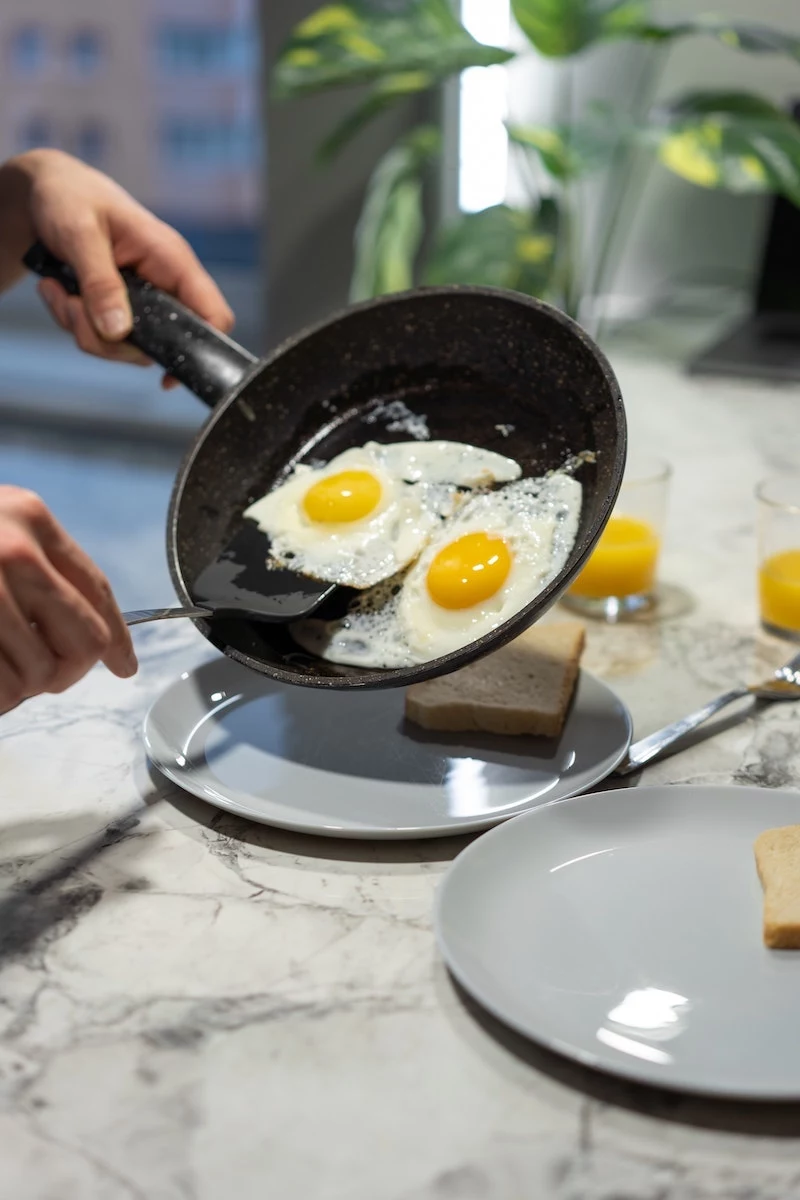 foods to eat in the morning person putting two eggs from a pan on a plate