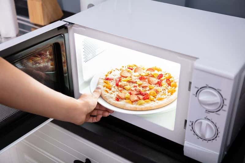 foods you should not reheat in a microvawe person putting pizza in the microwave