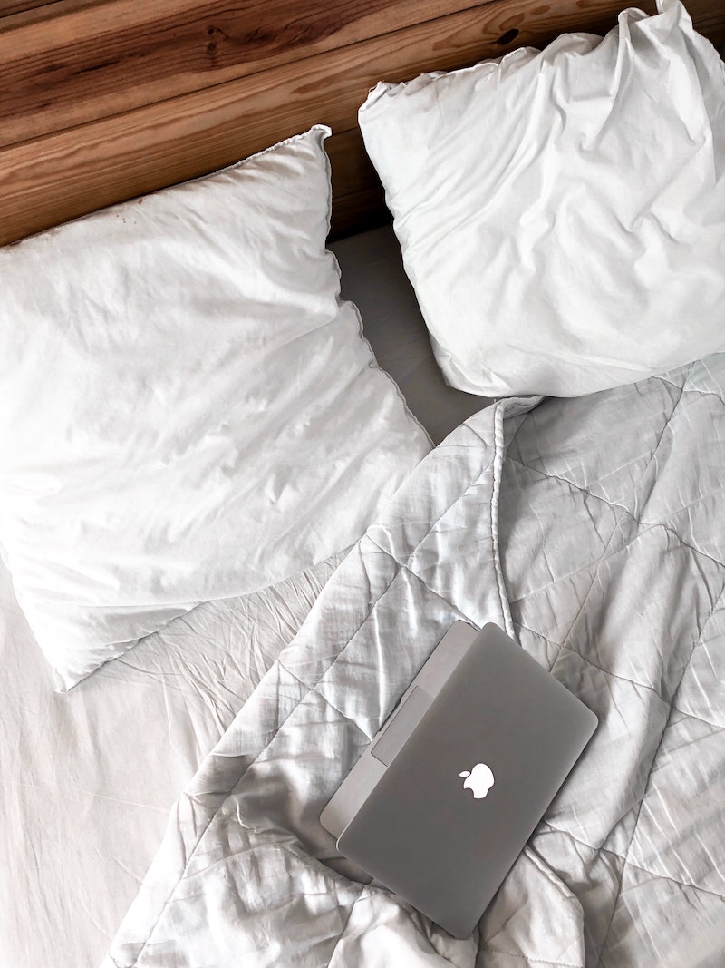 macbook open on white bed sheets