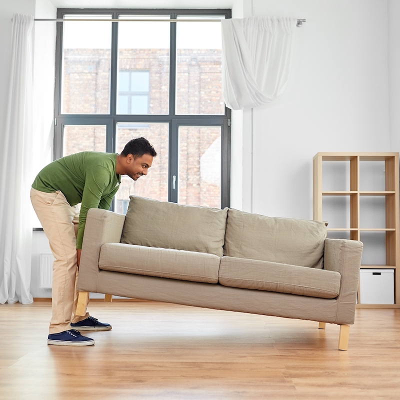 accommodation, furniture and interior concept happy indian man moving sofa at home