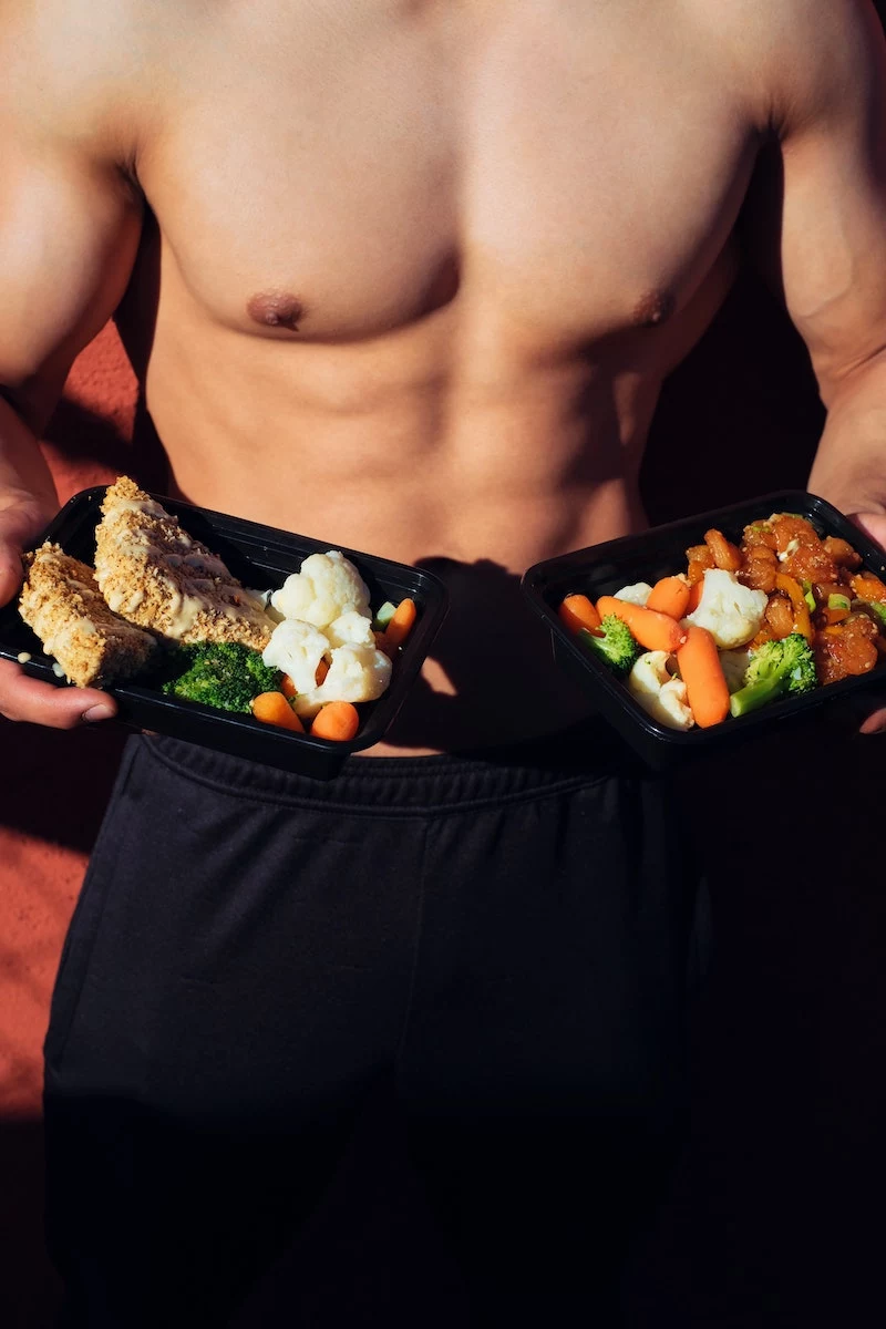 man with abs holding meal filled with vegetables