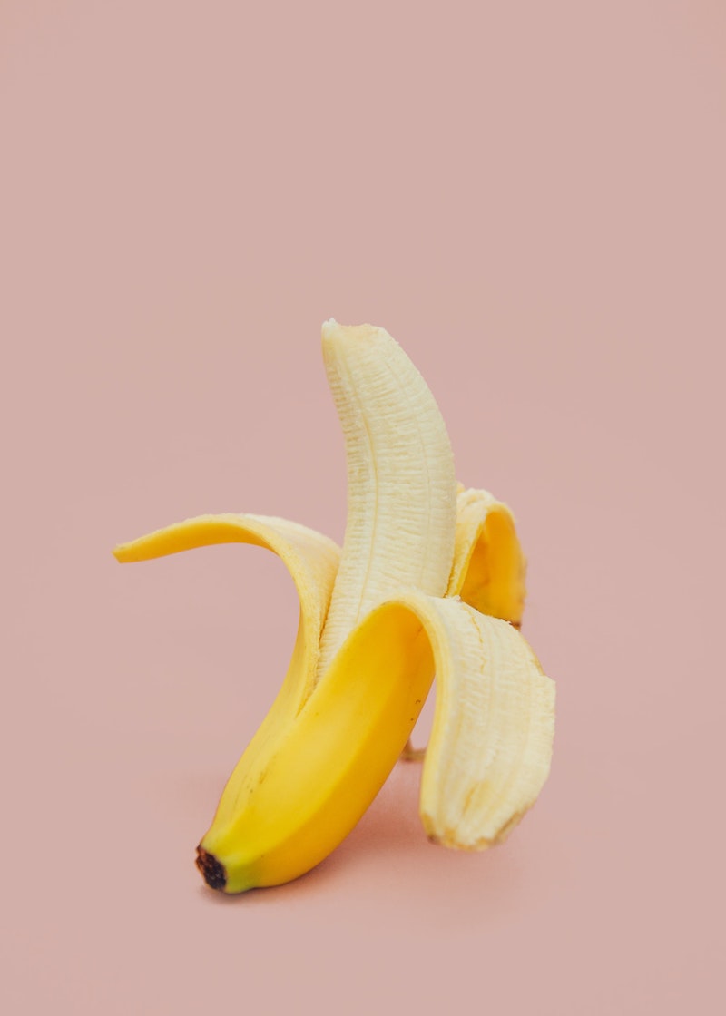 peeled banana halfway on pink background