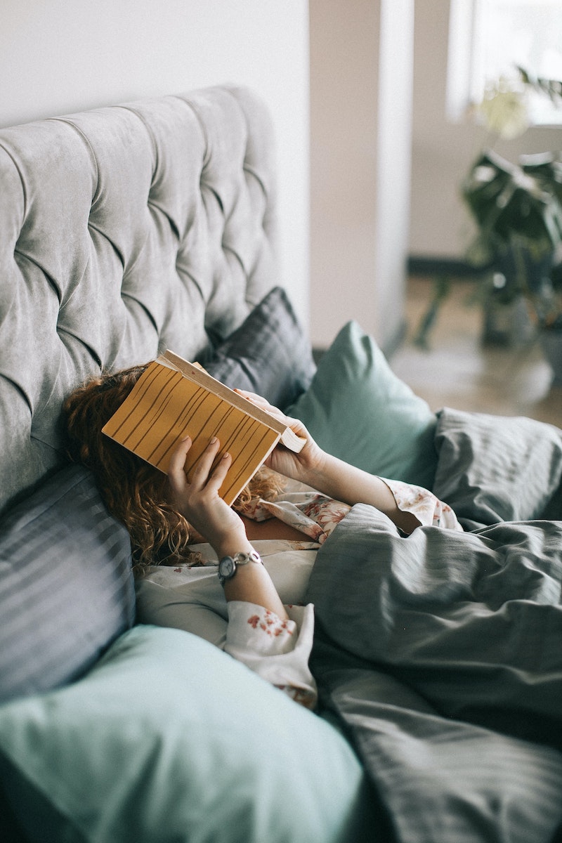 woman holding a book over her face in bed