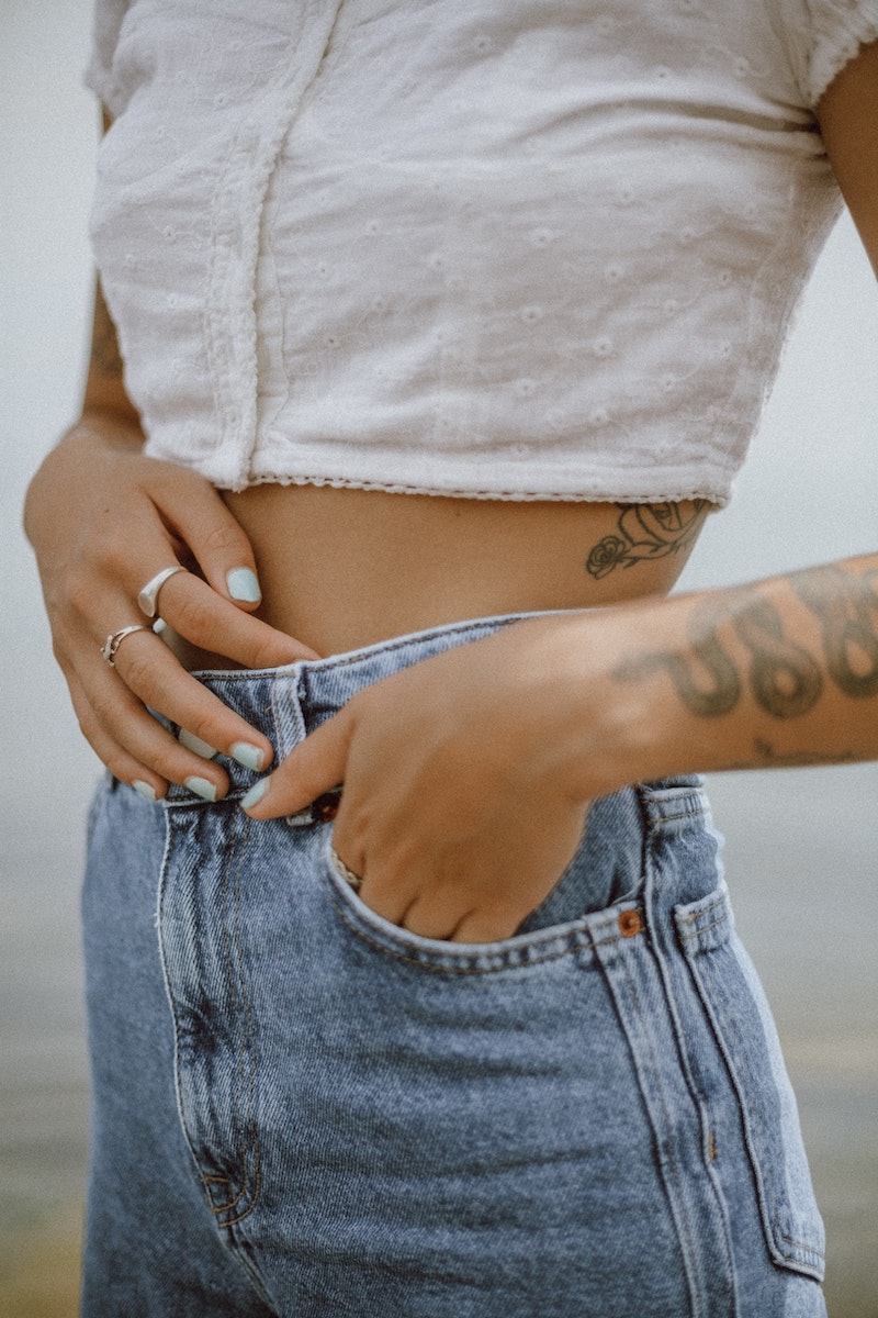 woman in jeans and white crop top holding stomach