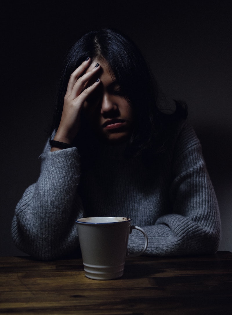 woman sitting in front of cup of coffee with head in hands