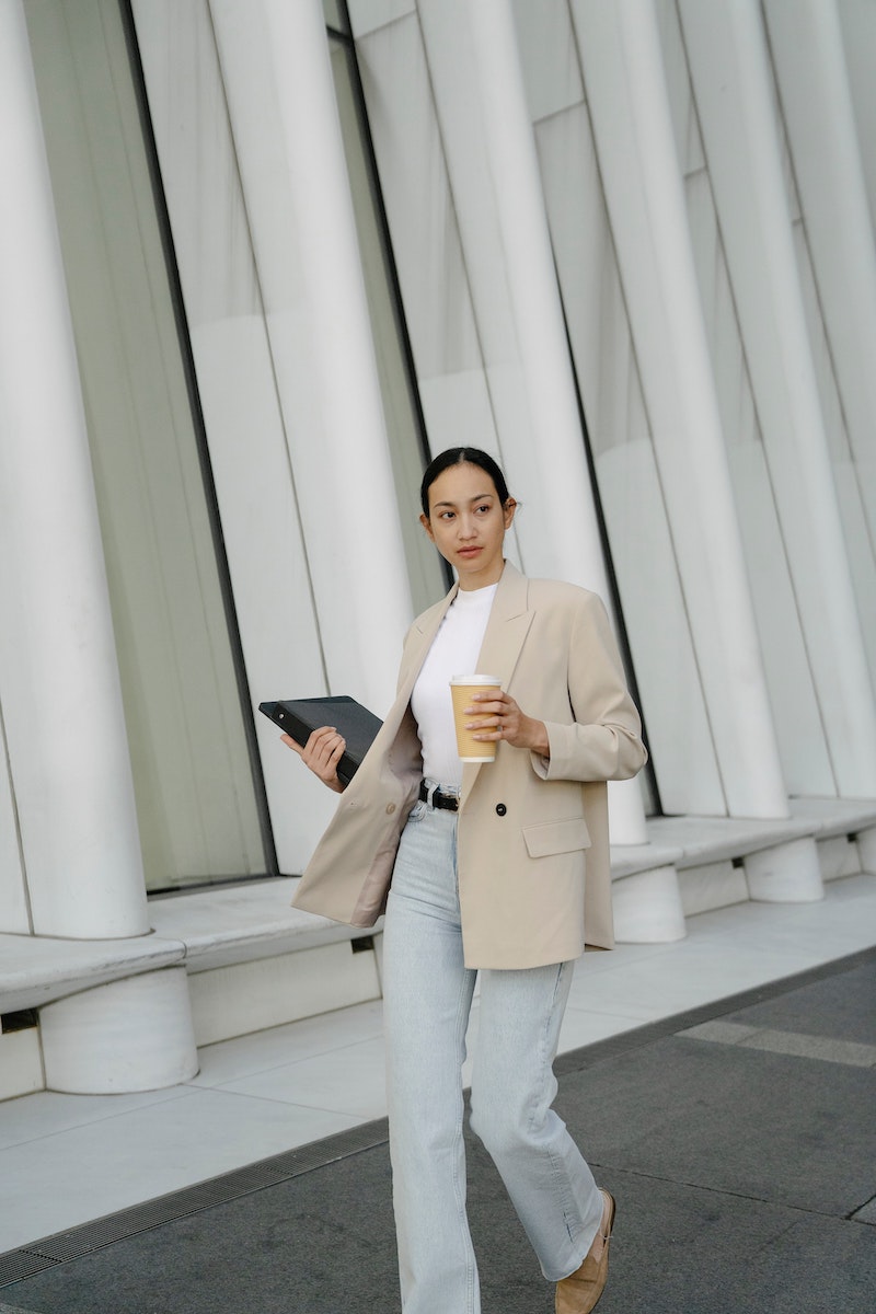 fall clothing essentials woman in jeans and blazer holding a coffee