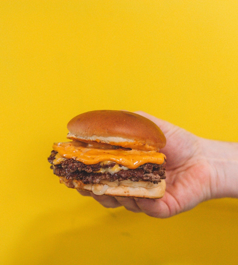 hand holding a cheese burger on yellow background