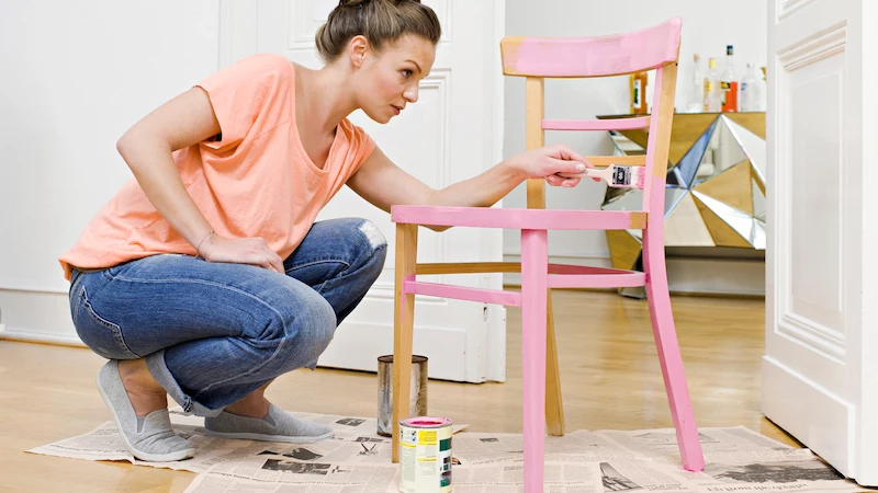 young woman painting wooden chair