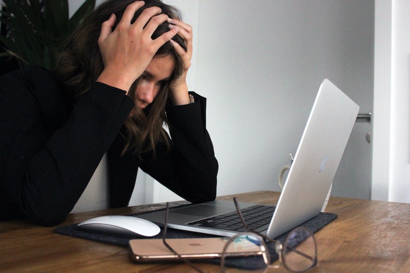 woman holding her head in stress above laptop
