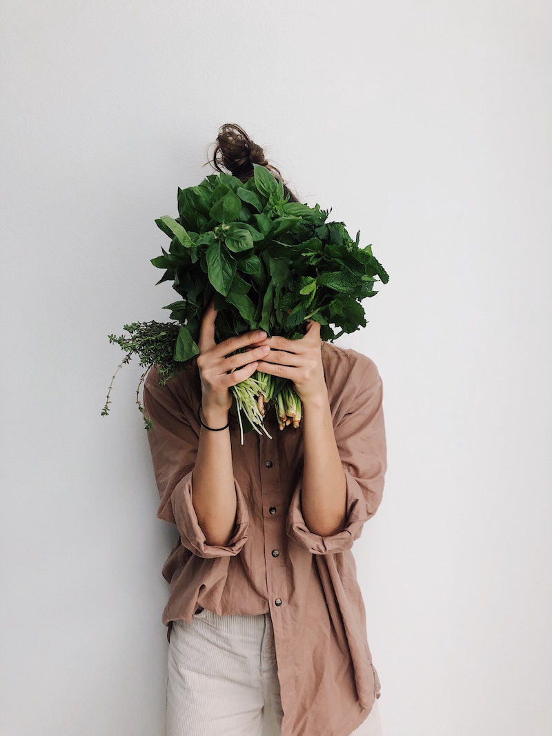 woman in brown shirt holding leafy greens