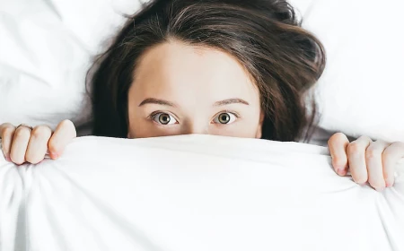 woman peaking out from the bed sheets