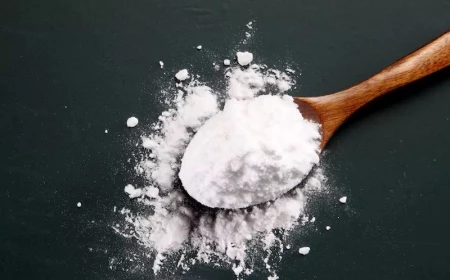 baking soda in wooden spoon spilt on black background