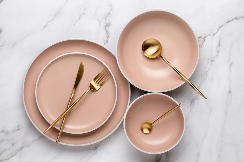 dishes utensils serving eating meals beige round rimmed plates gold colored cutlery white marble table top view modern ceramic crockery trendy