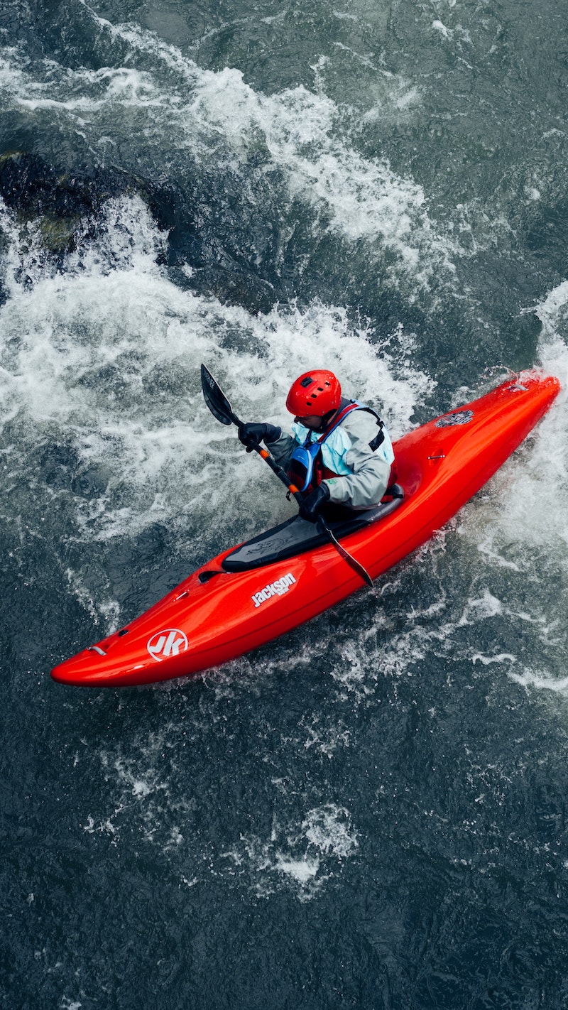 man kayaking on a red kayak rocky river