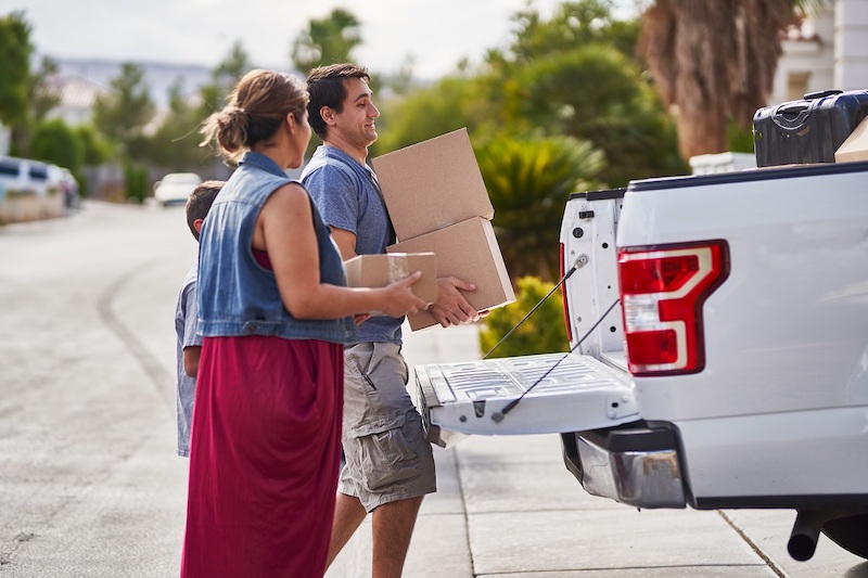 hispanic family moving boxes out of pickup truck into house