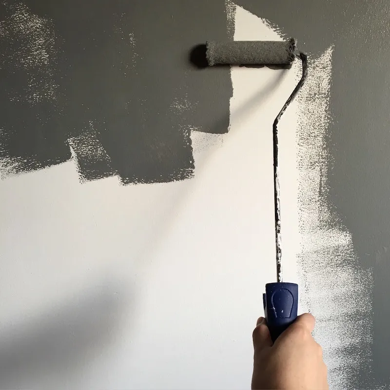 person painting a wall with roller in gray