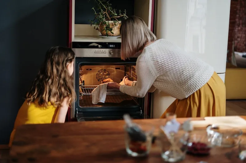 woman and young girl putting food in oven