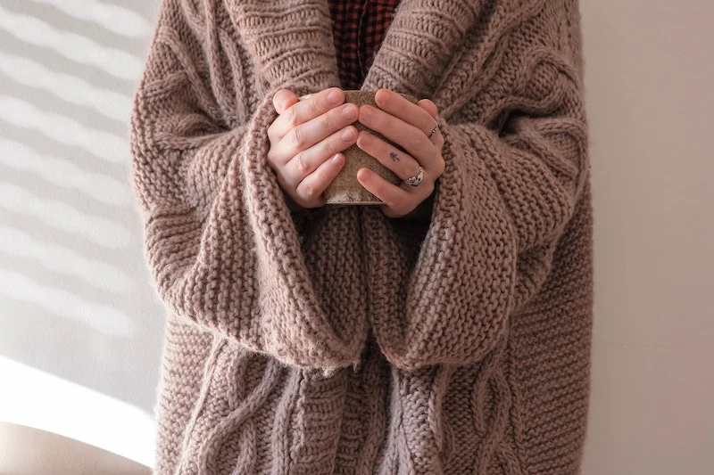 a person in a brown knit sweater holding a cup of tea