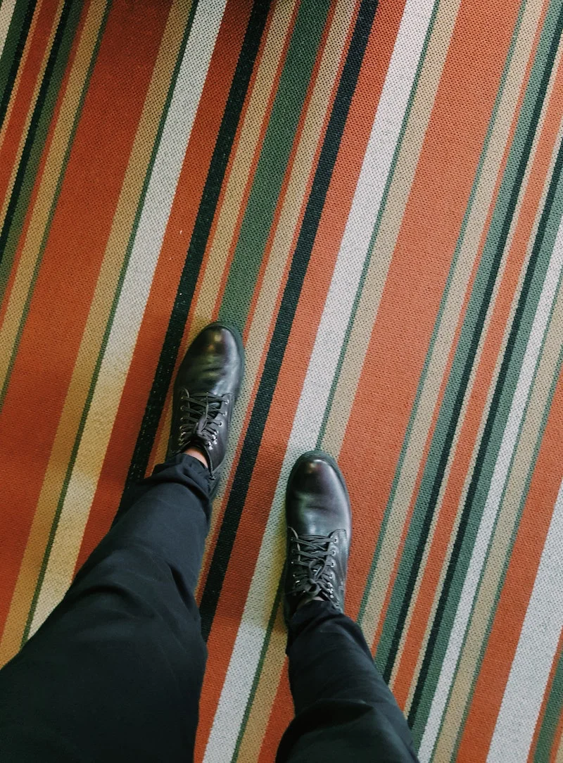 black shoes stepping on a colorful stripped carpet
