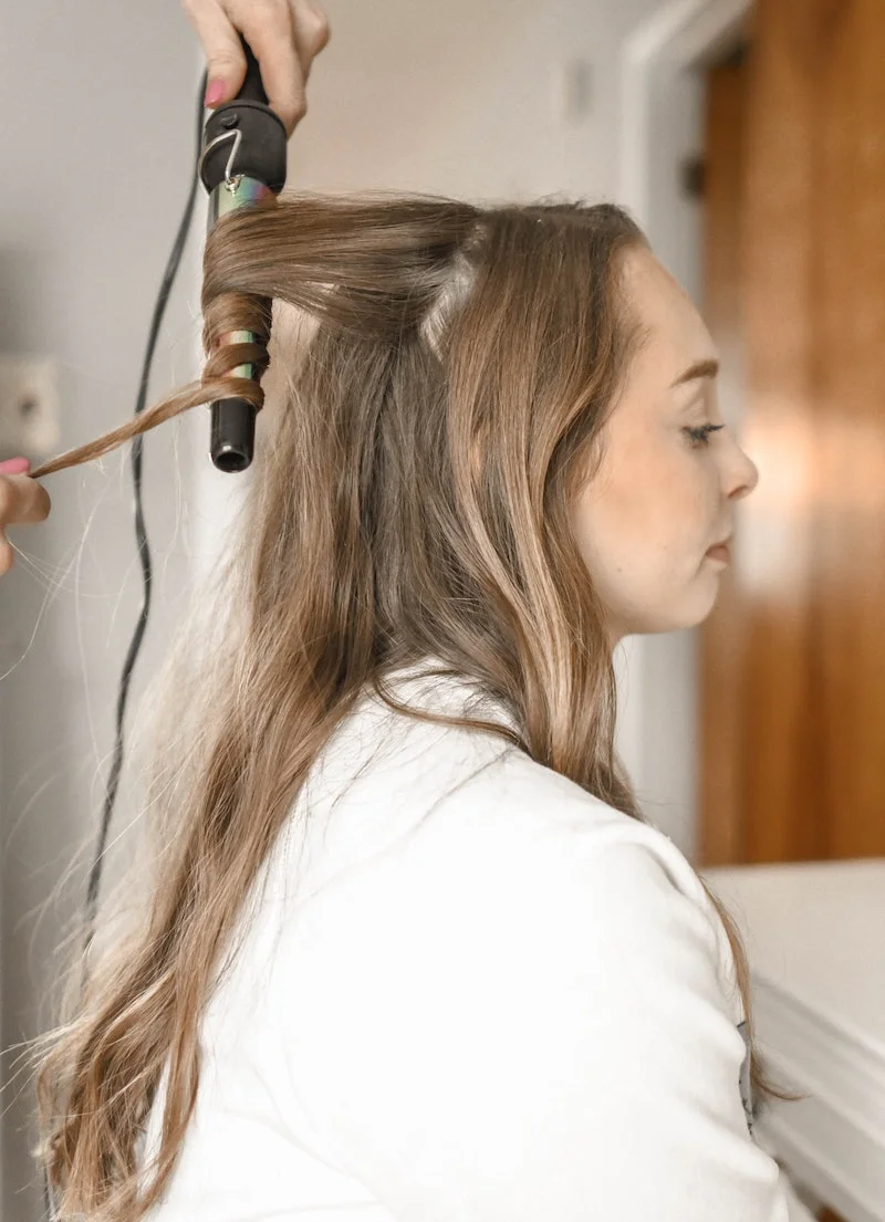 habits that are damaging your hair woman getting her hair curled with iron