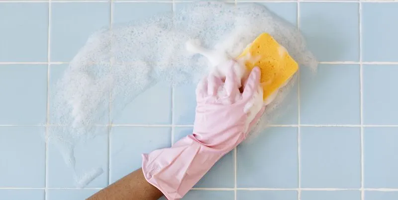 hand in pink gloves cleaning a blue tile bathroom