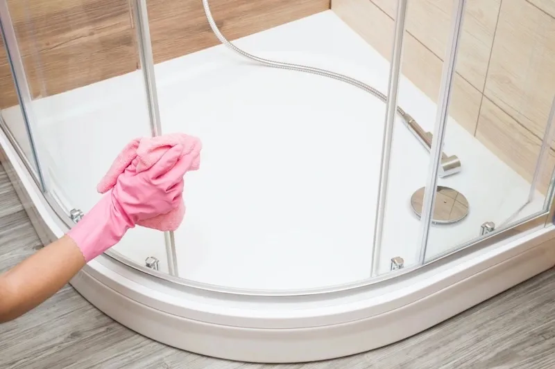 hand in pink gloves cleaning a shower