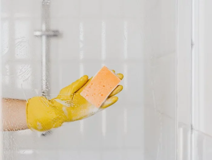 hand in yellow gloves cleaning a shower