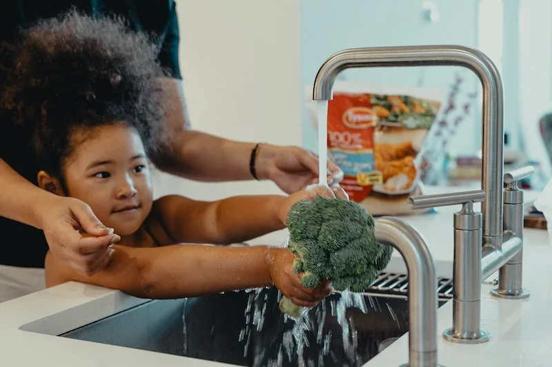 kid washing a broccoli under the sink