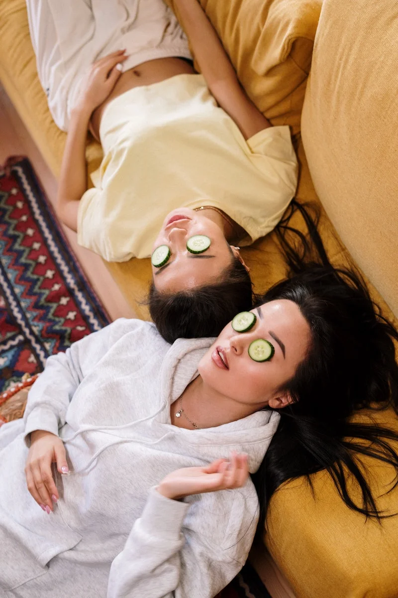 man and woman sitting and kaying with cucumbers on eyes